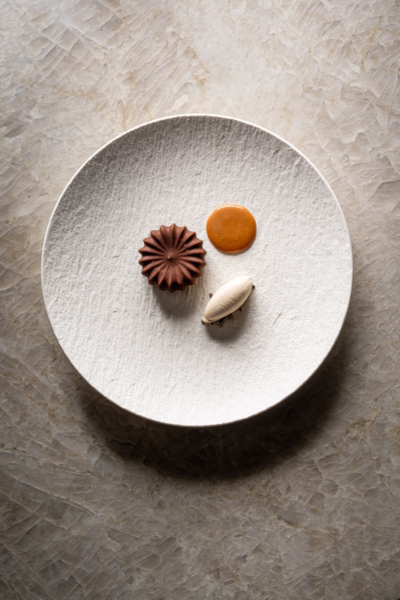 Dessert au chocolat, point de caramel et quenelle sur une assiette blanche texturée